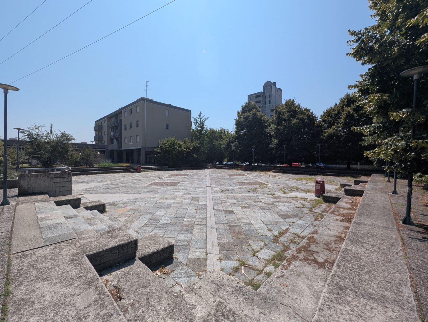 Piazza Caduti di Superga oggi: una superficie lastricata con gradoni in pietra, alberi sui bordi e le abitazioni sul fondo