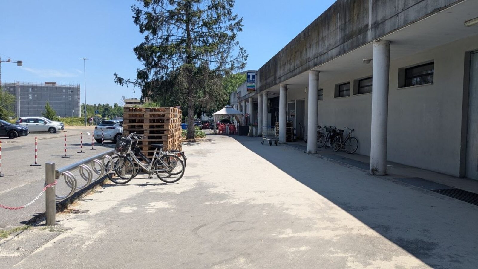 Il tratto di via Veterani dello Sport oggi: il portico dell'Emporio Solidale, una rastrelliera con alcune biciclette e il parcheggio a lato